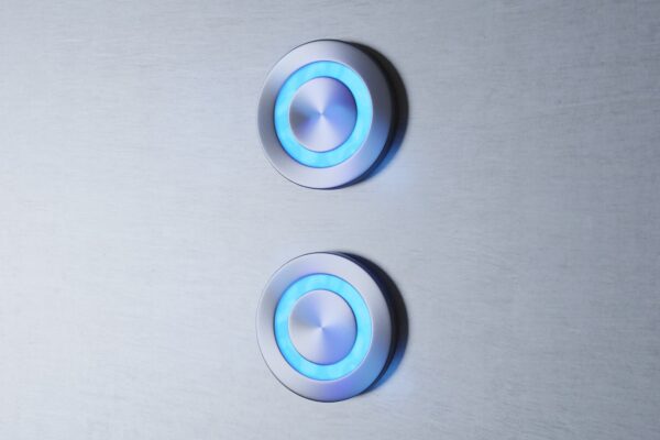 Two modern, illuminated Led Button GSL on a gray surface, emitting a soft blue glow around their circular metal frames.