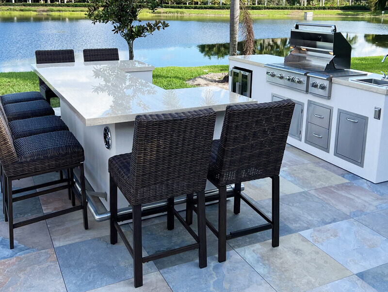 An image depicting the Maui 10 and GX10 Outdoor Kitchen featuring a GSL-32 Professional Grill, accompanied by accessories including refrigerator, sink, double side burner, and stools.