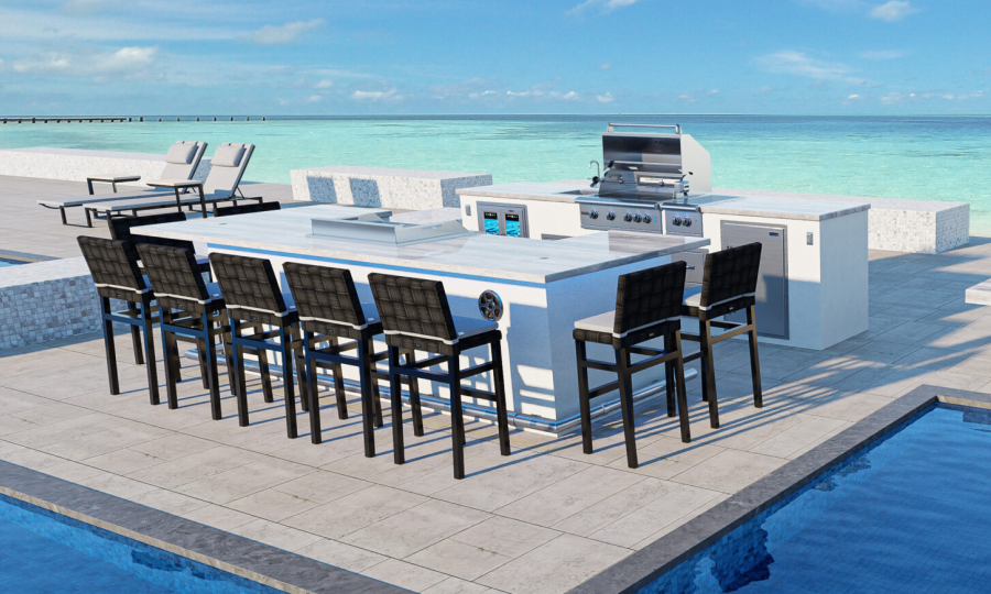 Outdoor kitchen setup featuring the MAUI 12 + GX12 CENTER white countertop island with eight tall woven bar stools. The kitchen includes a grill, side burner, and storage space, set near a pool overlooking a serene ocean view. In the background, a couple of lounge chairs face the water.
