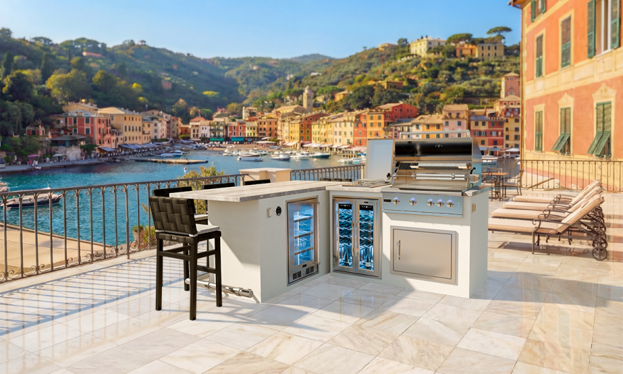 The PORTOFINO 7 + GX5 outdoor kitchen features a grill, fridge, and barstool on a tiled terrace with stunning views of a scenic coastal town, colorful buildings, boats, and lush green hills.