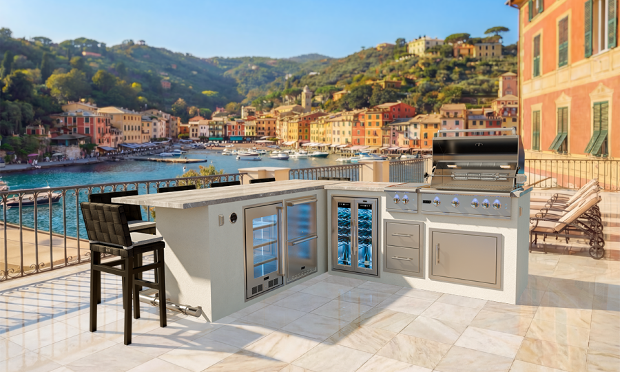 Enjoy the PORTOFINO 9 + GX6: a modern outdoor kitchen featuring a grill, bar seating, and built-in appliances on a tiled terrace with views of a coastal town’s colorful buildings and scenic waterfront hills.