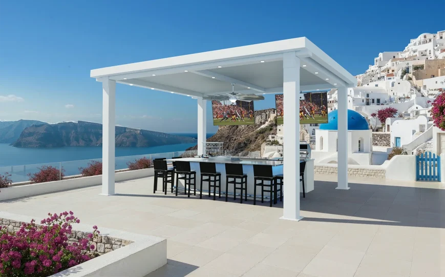 Enjoy the Mykonos (Copy): a modern outdoor patio with a white pergola, bar seating, and three TVs overlooking the sea and iconic blue-domed white buildings. Pink bougainvillea and cliffs complete this stunning coastal hillside view.